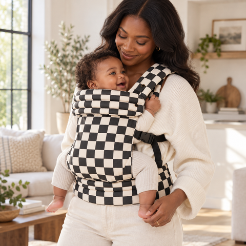 Mother carrying infant in the Née Checkerboard baby carrier at home