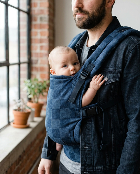 Father wearing draught board pattern ergonomic baby carrier with baby facing inward