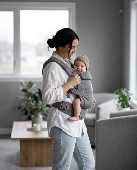 Mother wearing gray houndstooth ergonomic baby carrier with baby facing outward