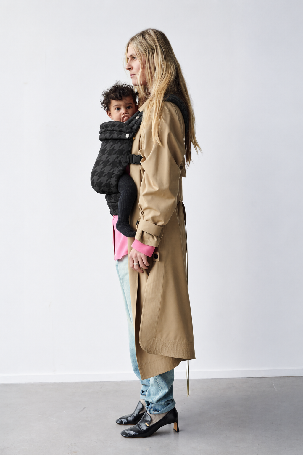 Full-length side view of a mother wearing the Née Denim Check ergonomic baby carrier with baby