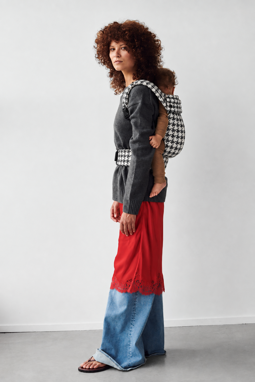 Mother wearing the Née Grand Houndstooth ergonomic baby carrier with baby in a back carry