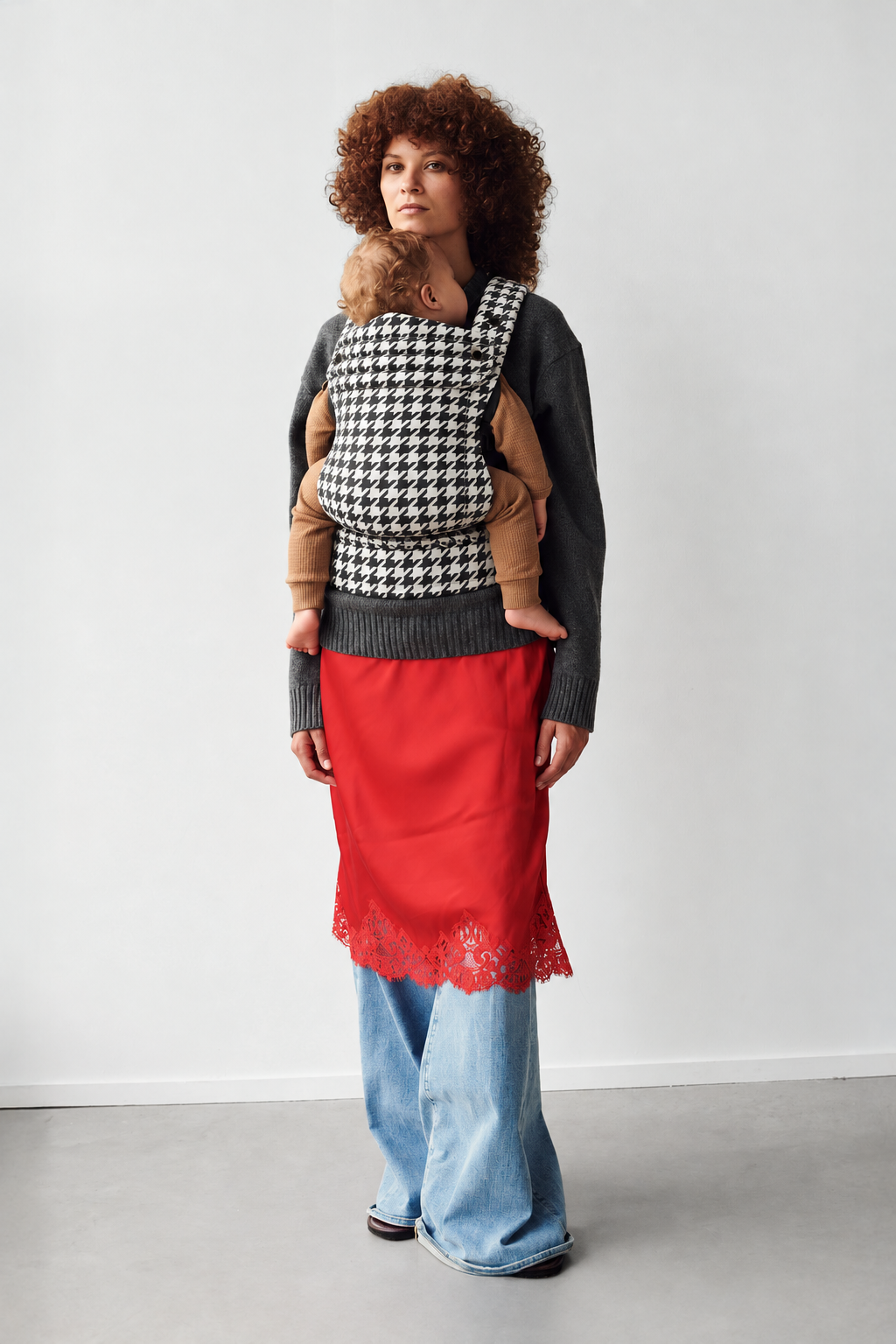 Mother wearing the Née Grand Houndstooth ergonomic baby carrier with baby, full-length view