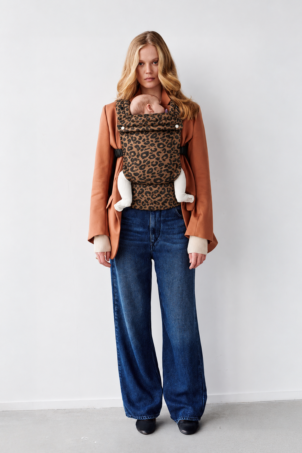 Blonde mother wearing the Née Leopard Print ergonomic baby carrier with baby, full-length view