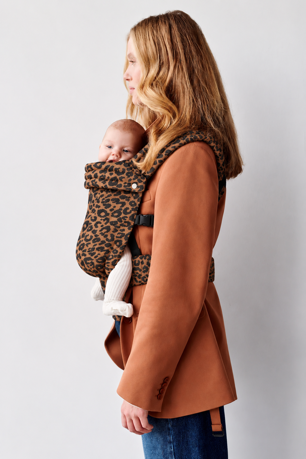 Side view of a blonde mother wearing the Née Leopard Print ergonomic baby carrier with baby