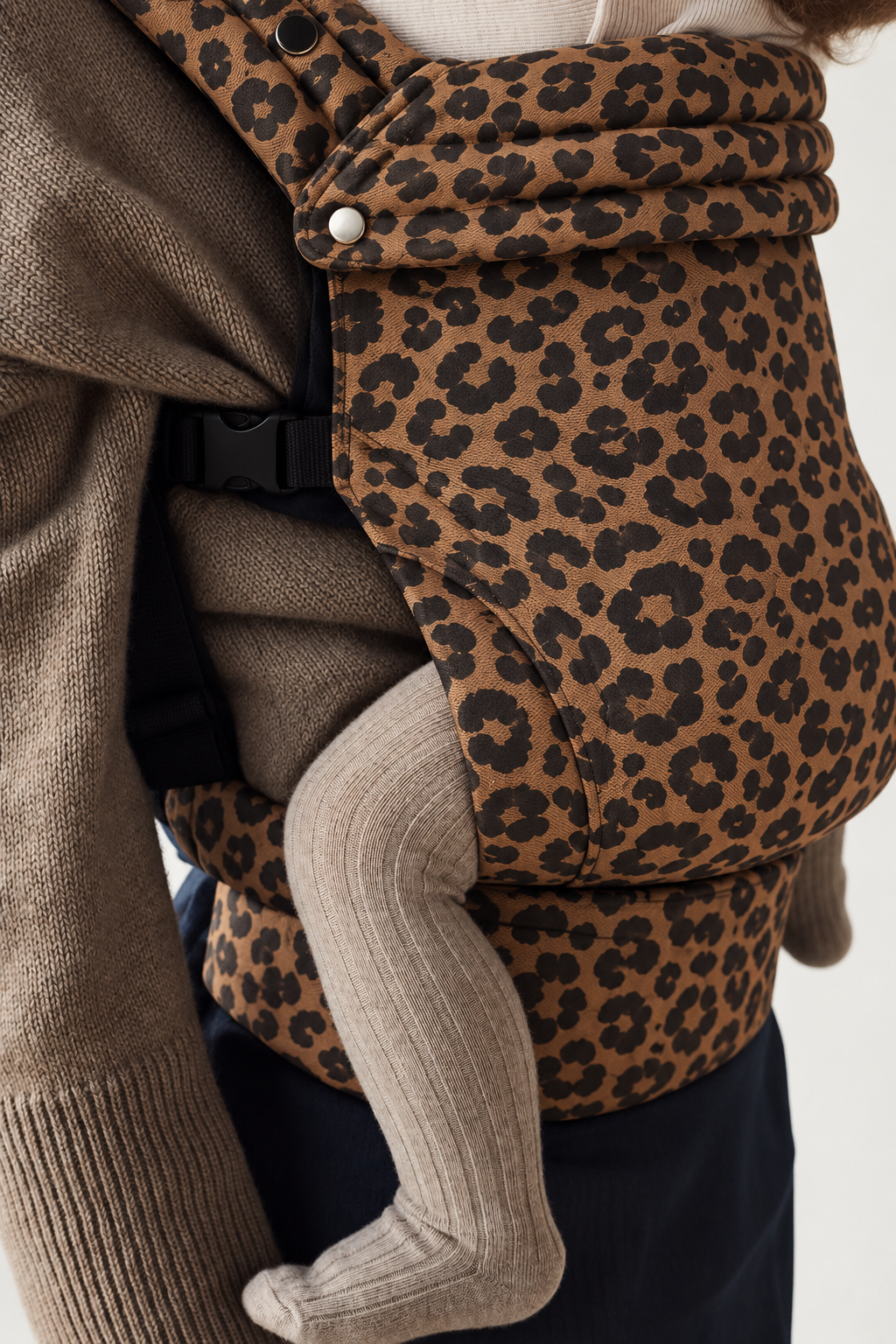 Close-up of the Née Leopard Print ergonomic baby carrier fabric, waistband and baby