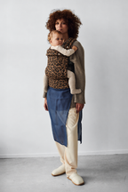 Mother wearing the Née Leopard Print ergonomic baby carrier with baby, full-length view