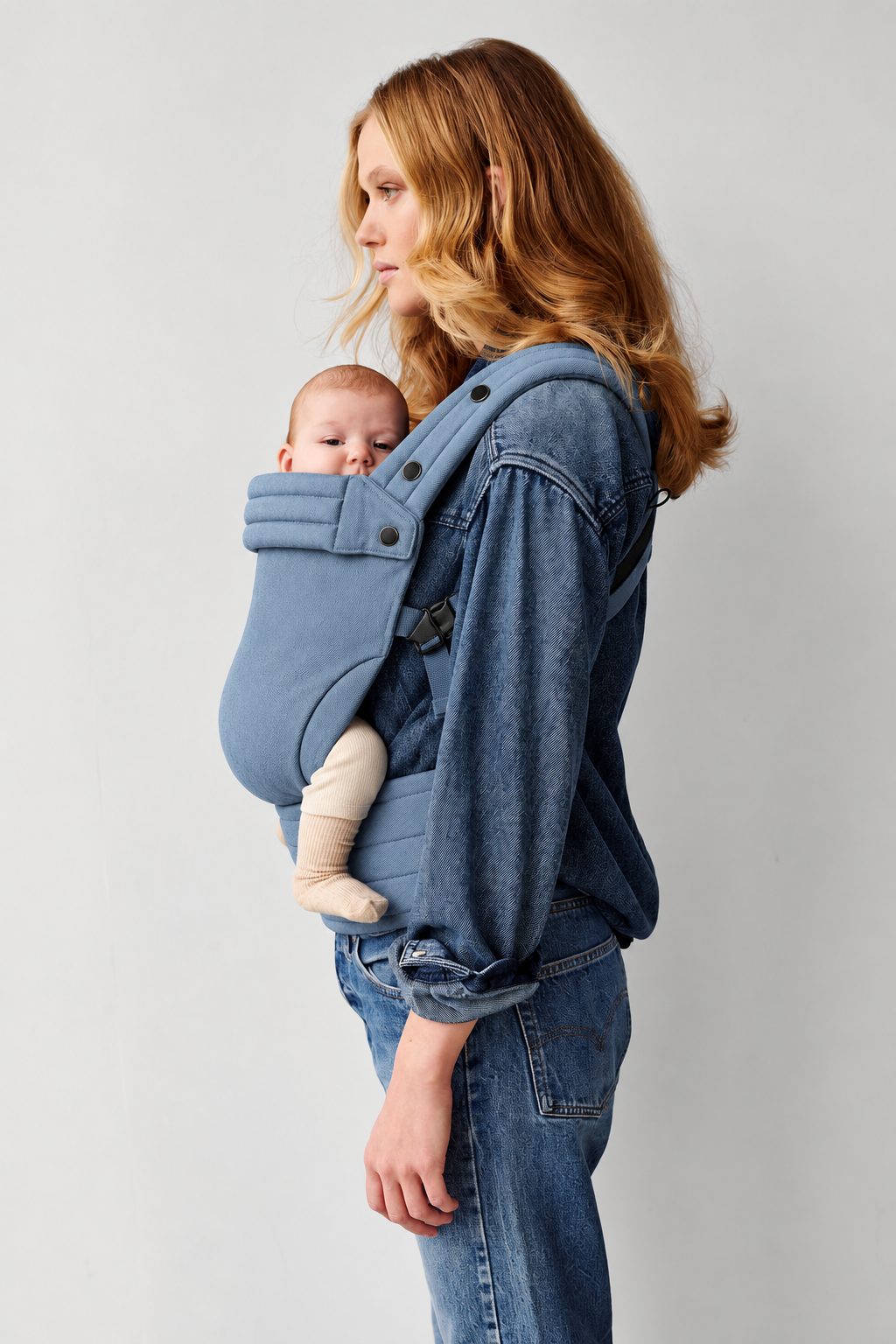 Side view of a mother wearing the Née Powder Blue ergonomic baby carrier with baby